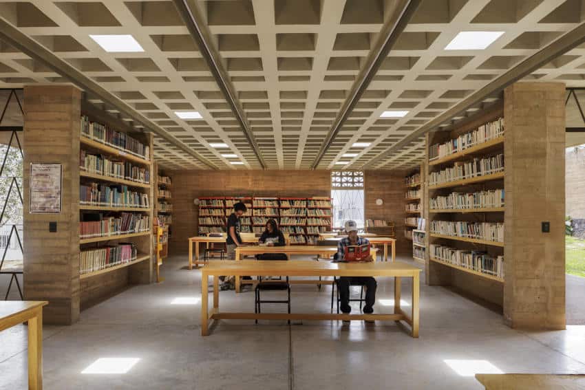 Jiutepec, Morelos, residents sitting at wide wooden tables in a library space surrounded by shelves filled with books.