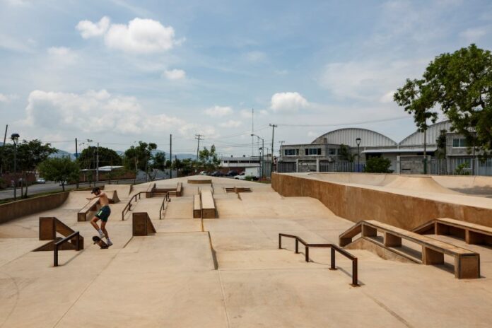 Man in shorts and no shirt in Jiutepec, Mexico, doing tricks on a skateboard in a skate park. There are no other people in the park.