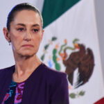 Claudia Sheinbaum with a serious expression and a Mexican flag