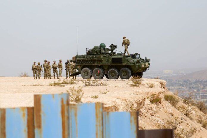 A US military tank and troops on a bluff behind the Mexico-US border wall