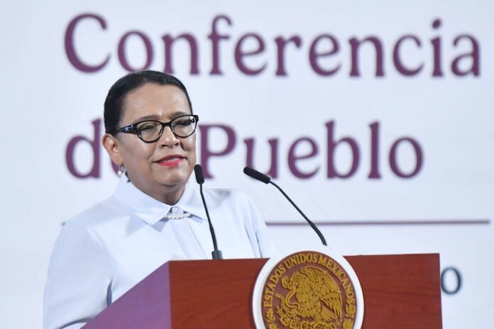 A dark-haired woman speaks at a podium emblazoned with the emblem of the Mexican government.