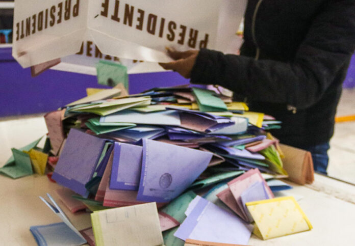 A person dumps a box of votes onto a table