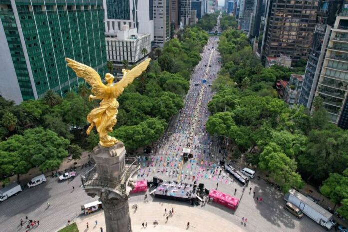 An aerial view of the Angel of Independence monument on Reforma Avenue in Mexico City, looking down the tree-lined boulevard surrounded by tall city buildings.