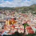 I’ve seen Latin America, but Mexico’s still my favorite country for retirement An expansive panoramic view of Guanajuato City, Mexico, showcasing its vibrant, colorful houses covering rolling hills, with prominent landmarks like the yellow Basílica Colegiata de Nuestra Señora de Guanajuato and other historic buildings, under a partly cloudy sky.