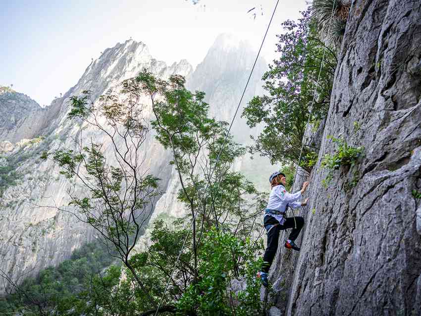 A rock climber ascends a sheer limestone wall at El Potrero Chico, Mexico, with dramatic peaks in the background.