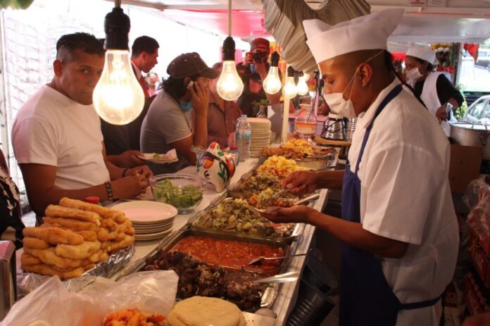 Mexico City residents standing and sitting at a temporary taco stand while waiting for employees to fill their tacos with cooked items in buffet trays.
