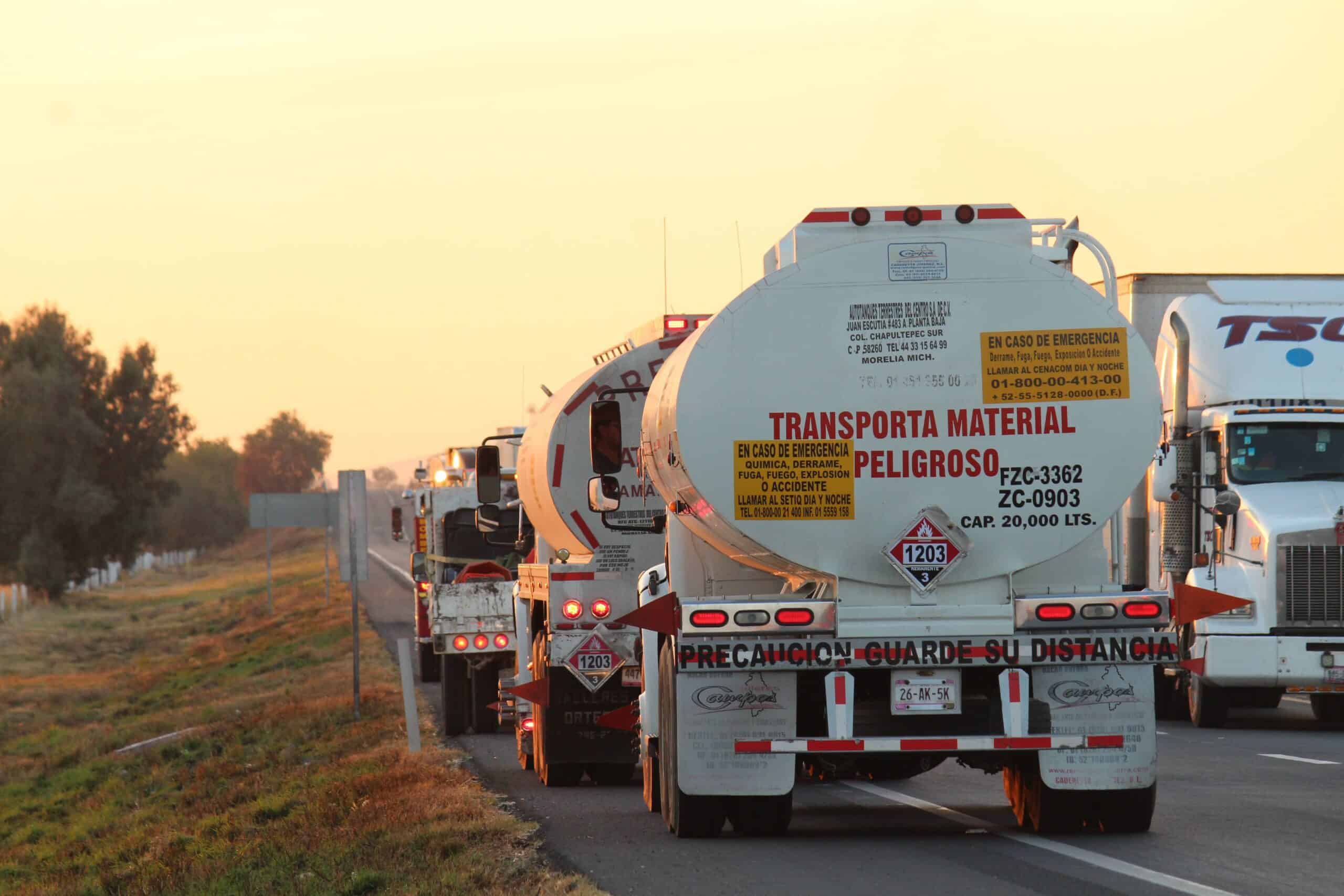 Oil tankers drive down a highway at sunset