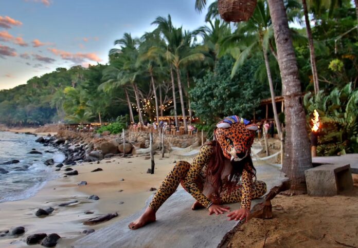 A woman in jaguar mask sitting on a beach