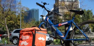 A blue mountain bike with a Rappi food delivery backpack case, both chained to a post in Mexico City.