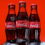 The relentless imperialism of Coca Cola and our rights to health Three bottles of Coca-Cola on a pile of ice cubes and against a red background.