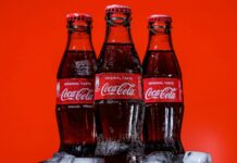 The relentless imperialism of Coca Cola and our rights to health Three bottles of Coca-Cola on a pile of ice cubes and against a red background.