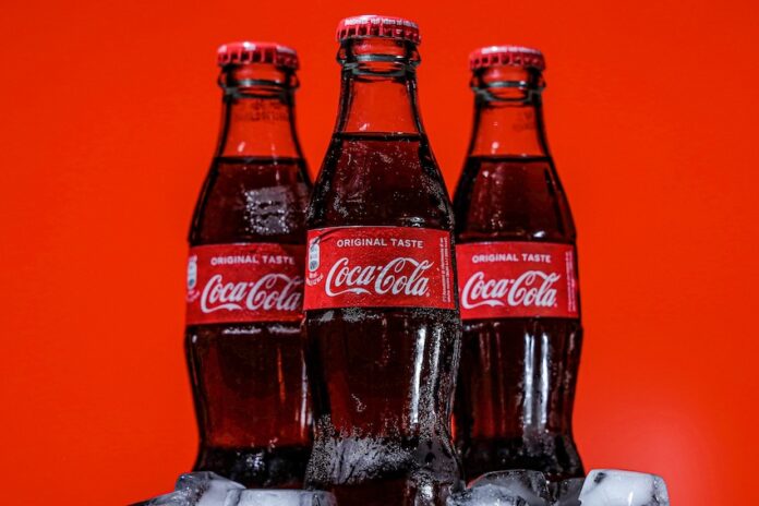 Three bottles of Coca-Cola on a pile of ice cubes and against a red background.