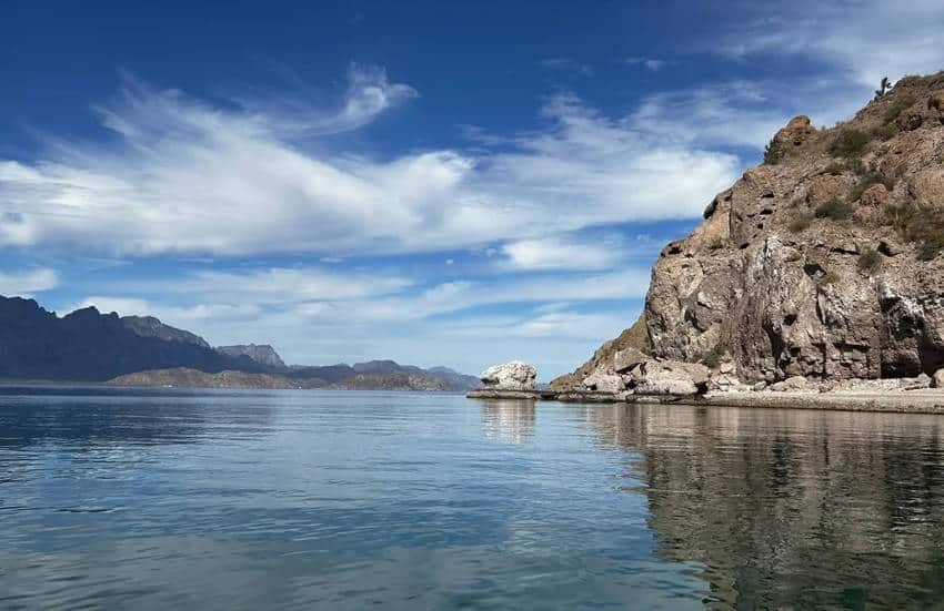 Calm blue waters of the Gulf of California with rocky islands and a rugged coastline under a partly cloudy sky