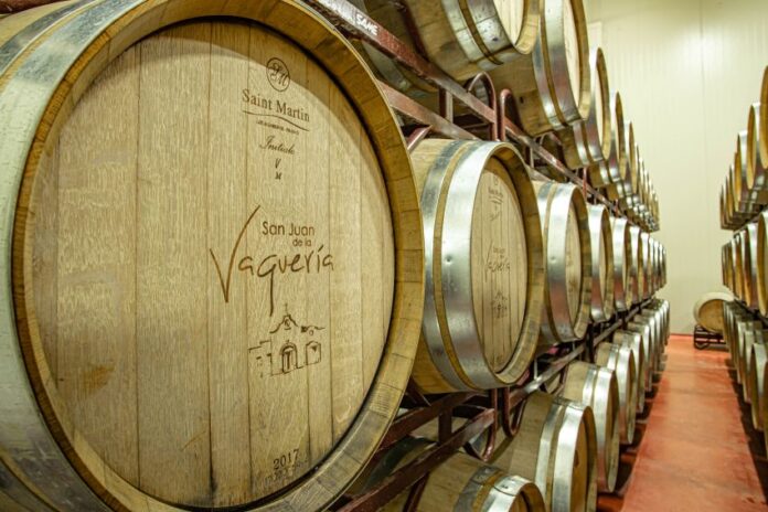 Two shelves with three rows each of wooden wine barrels with metal around their lids.