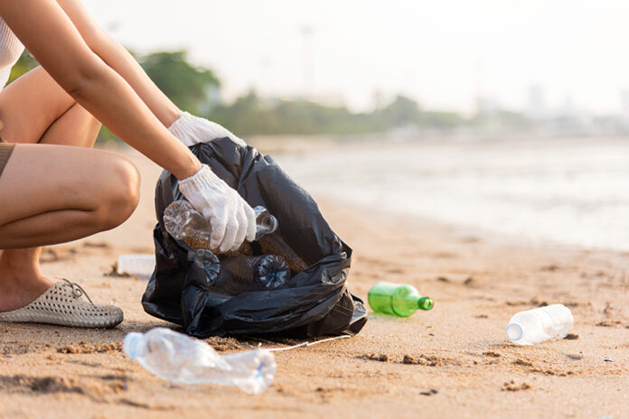 A woman picks up plastic bottles on a beach