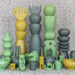 How a Mexico City studio is championing truly fair artisan partnerships A collection of unique, handcrafted Mexican ceramic art pieces in shades of green and yellow, including tall stacked sculptures, vases, bowls, and whimsical figures, arranged on a textured grey surface.