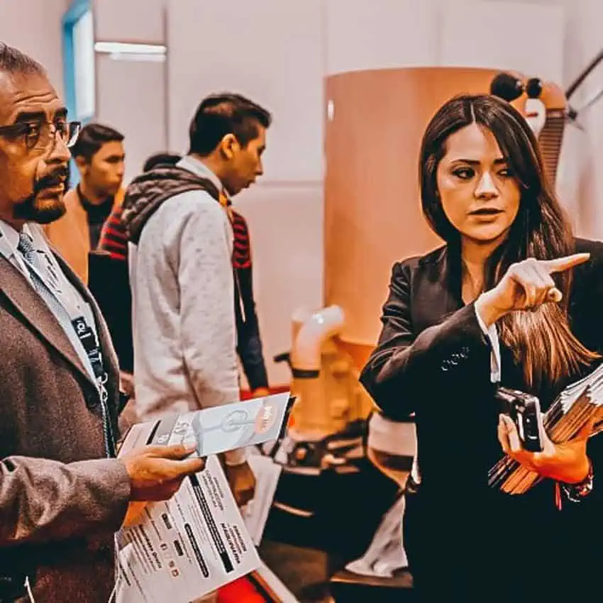 A group of people indoors at the Cihac real estate industry expo in Mexico. A woman is pointing off camera as if giving directions to the man in front of her.