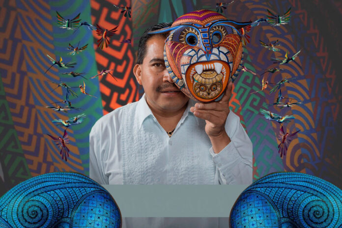 Artist Jacobo Ángeles holding a traditional Oaxacan folk art mask in front of his face.