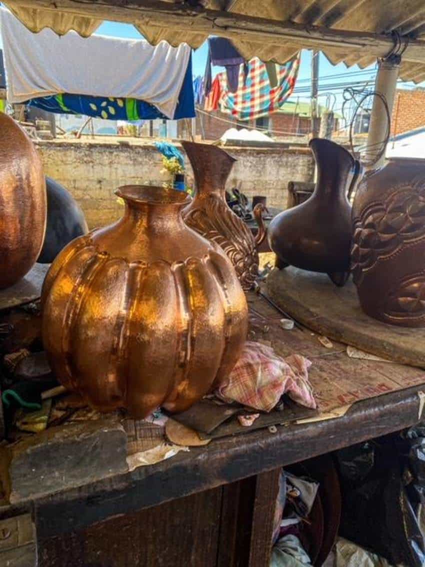 five copper-hammered pots in various stages of completion sitting on a wooden outdoor table in a covered partly workshop