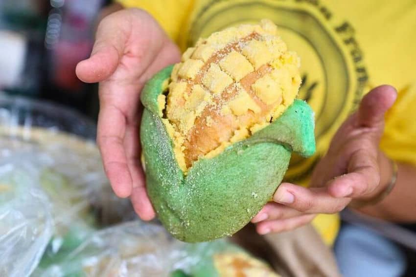 Hands hold green and yellow pastry shaped like a fat, stubby ear of corn.