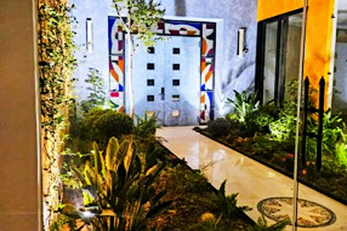 A modern Mexican courtyard with parquet floor and stone double entrance doors to a home. The three sides around the doors feature modernist abstract colors of stained glass.
