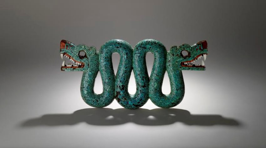 A wooden and turquoise scuplture of a double headed snake against a blank, empty background, as is often done in photography by art museums or auctions.