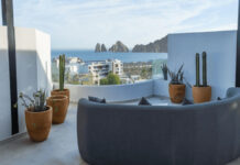 Want to buy property in Mexico? Make sure you invest close enough to a major airport A modern rooftop patio features a curved grey sofa, potted cacti, and a panoramic view of the ocean, a city, and distant rock formations under a clear sky.