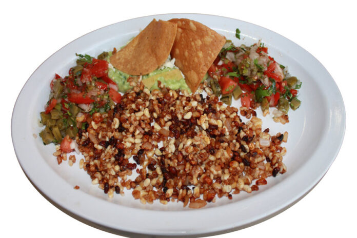 A white plate with escamoles at the center, with chips, guacamole and salsaon the side