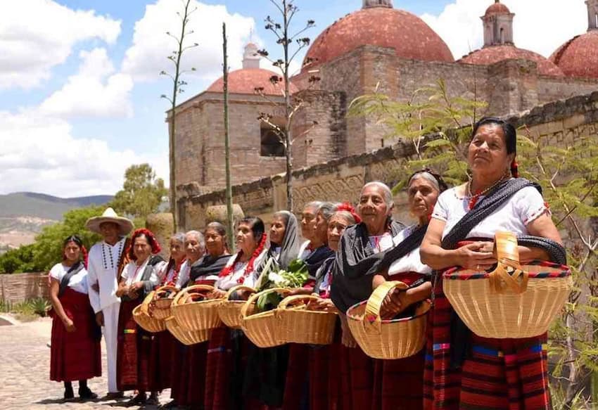 A group of elderly women stand in a line, holding baskets of food.