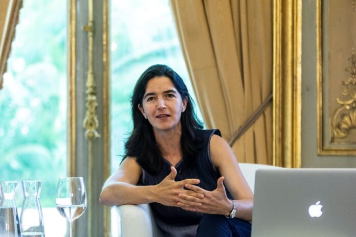 Mexican architect Fernanda Canales sitting at a luxurious wood table with small, glass water pitchers and a wine glass half filled with water.