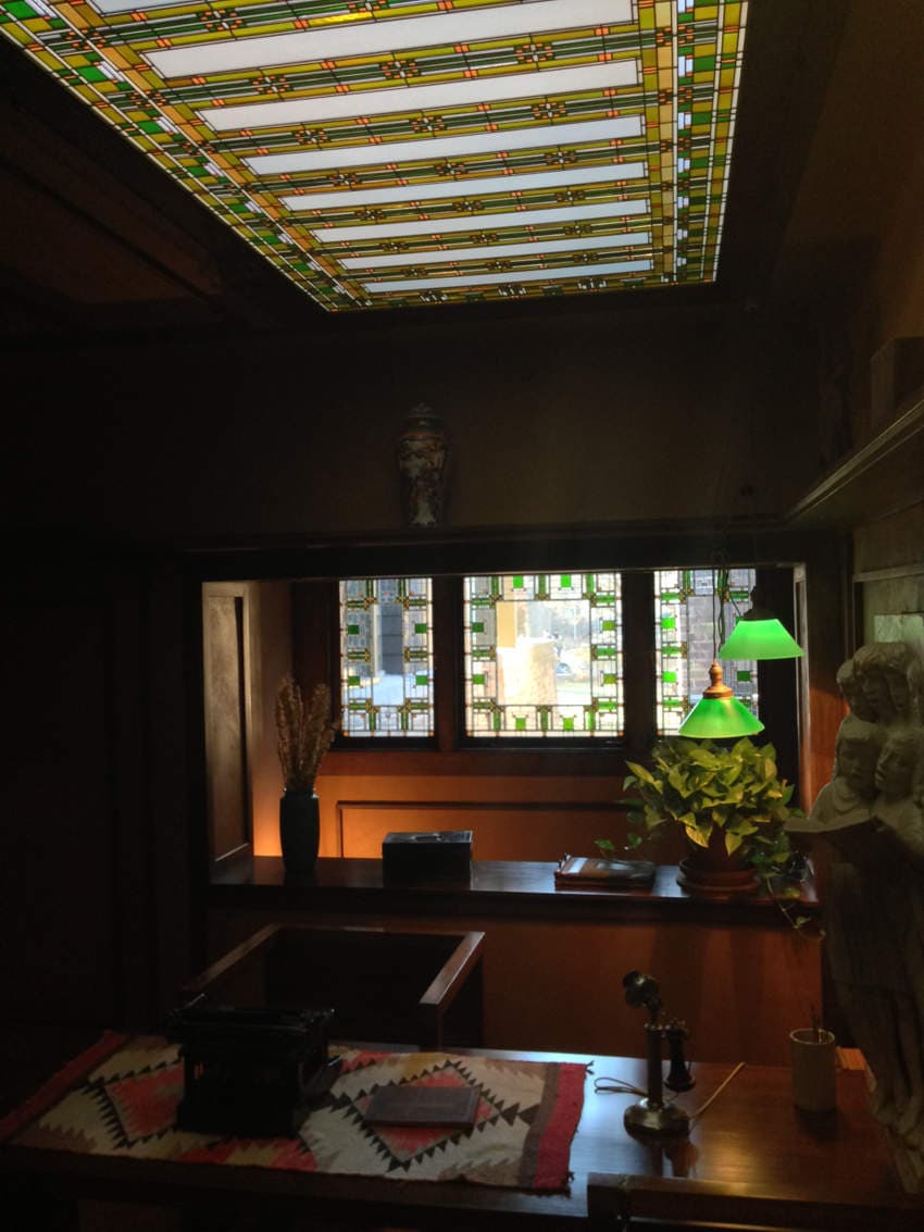 A dark studio with a desk, glass lampshades, and stained glass windows in the ceiling and in the front of the room.