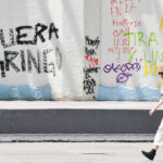 A blonde woman walks past graffiti reading "Fuera gringo" in Mexico City