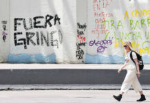 A blonde woman walks past graffiti reading "Fuera gringo" in Mexico City
