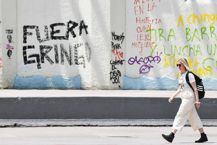 A blonde woman walks past graffiti reading 