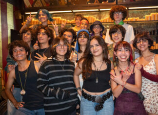 Retirement mecca San Miguel de Allende changes its tune with increasing youth activities A diverse group of smiling Mexican teenagers, with various hairstyles and clothing styles, pose for a group photo in a dimly lit restaurant or bar with rows of candles in the background.