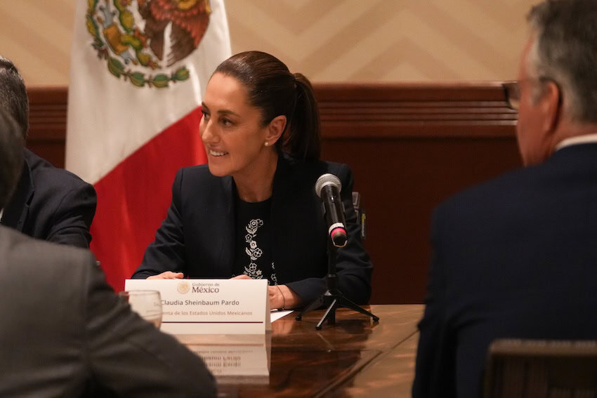 President Sheinbaum seated in front of Mexican flag