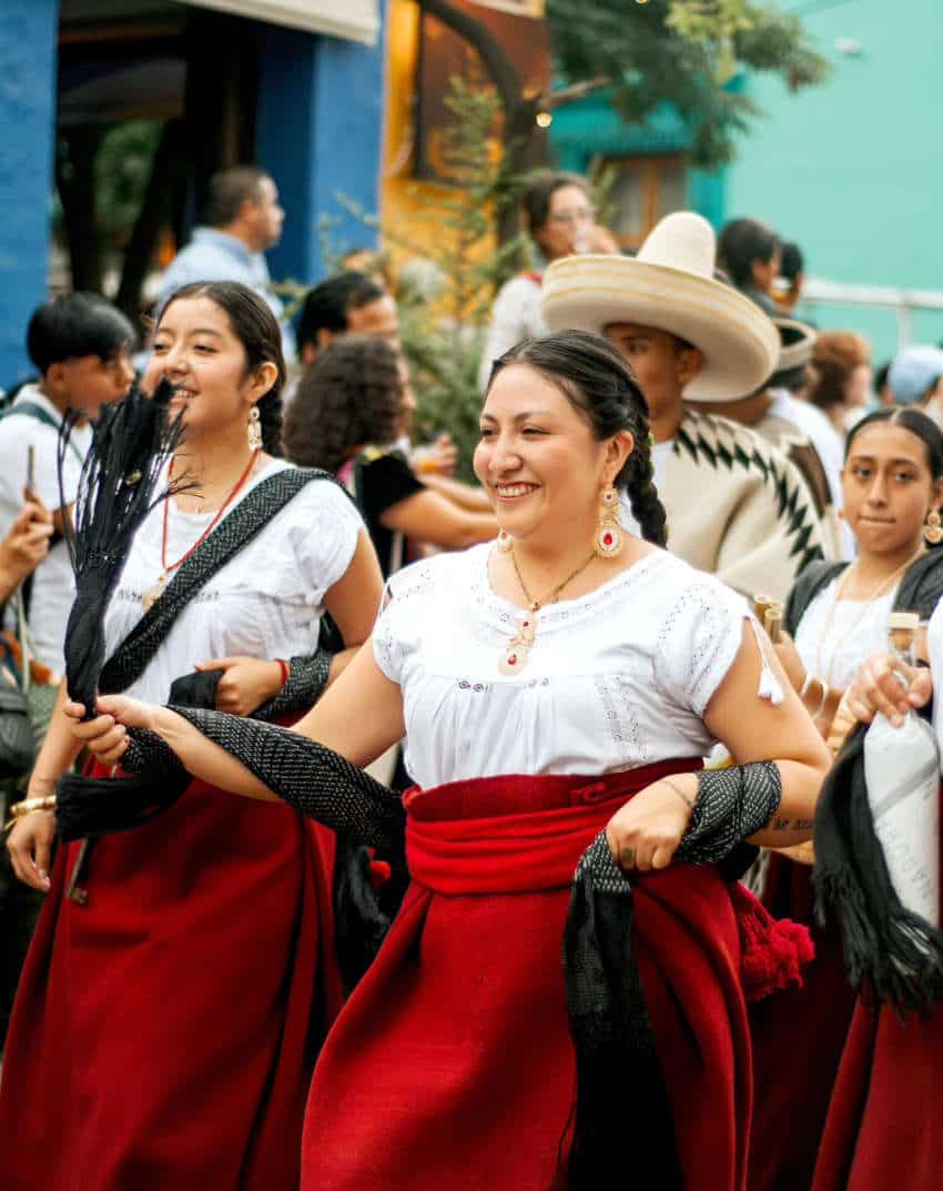 Mexican men and women in traditional red and white attire dancing during Oaxaca city's Guelaguetza festival.