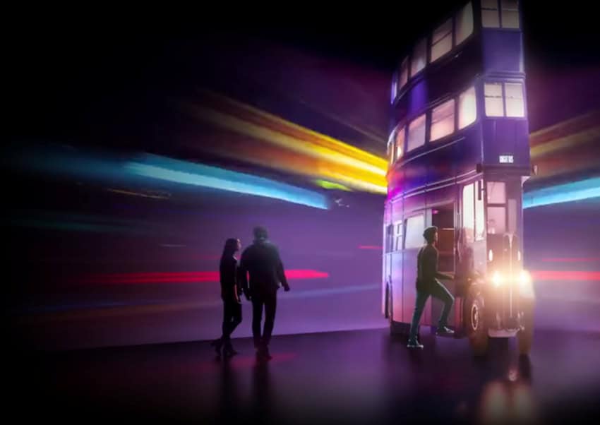 Museum exhibit featuring a replica of a classic London double-decker bus, surrounded by streaking light trails that create a sense of motion and energy. Purple and magenta lighting bathes the entire scene. A male and female couple are in the background walking together through the exhibit.