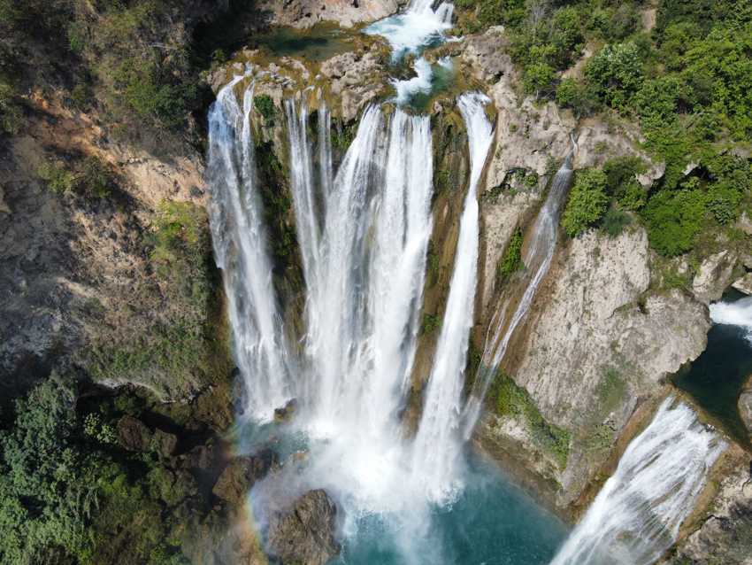 Aerial view of multiple streams of a waterfall cascading down into a turquoise pool in the Huasteca Potosina region of Mexico.