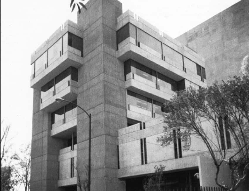 A monolothic gray concrete building with five floors with windows on every side of the building