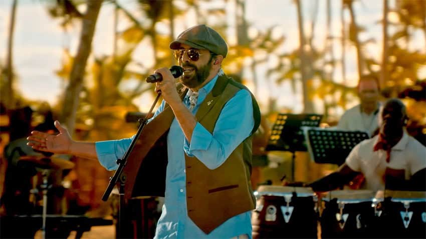 Juan Luis Guerra sings with a band at sunset in front of palm trees
