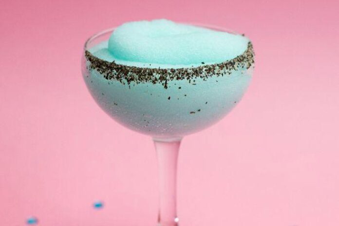 A fluted cocktail glass with a light blue frozen cocktail