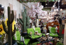 Toilets with sinks and neon dog sculptures: The kitschy appeal of Galerias El Triunfo A vibrant Mexican-themed home decor display featuring large artificial cacti, bright green patio furniture, sunflowers, a cow statue, and various rustic lanterns and lighting fixtures, suggesting an eclectic outdoor living space.