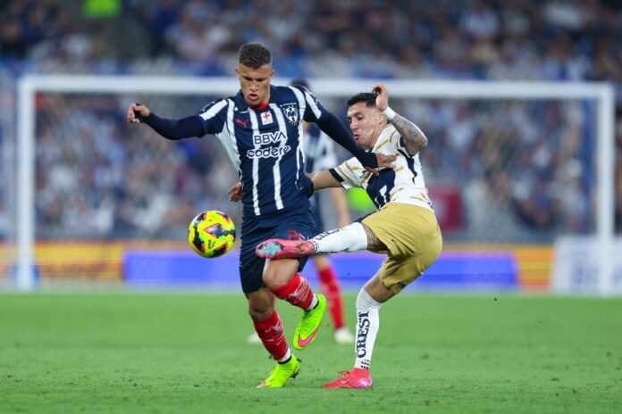 Two soccer players in Mexico in a heated bid for control of the ball during a stadium game. One man is trying to kick the ball away from the other player, who is holding him back with his hand.
