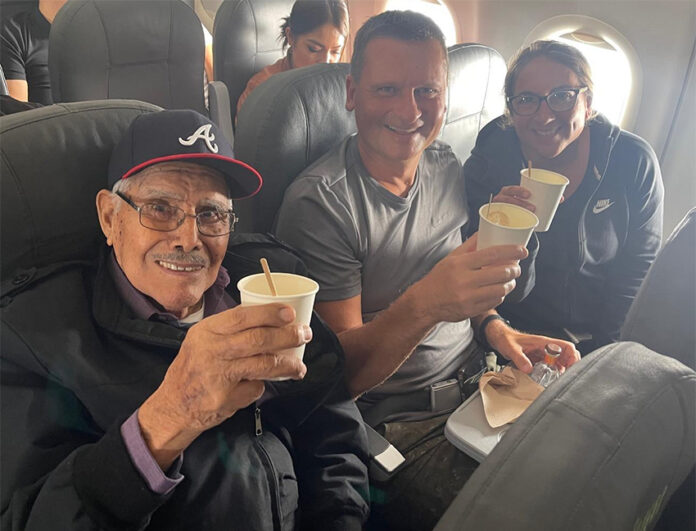 Travis and Tamanna Bembenek raise styrofoam cups to toast with Luis, an elderly Mexican man, on a plane