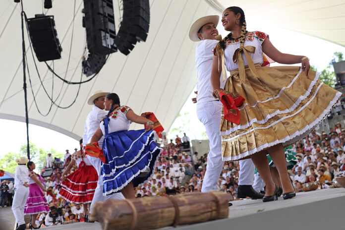 Dancers in traditional garb including long colorful skirts dance on a stage a Guelaguetza in Oaxaca