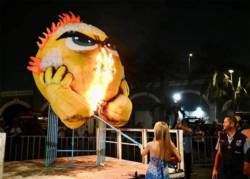 A woman with a long torch sets light to a giant effigy of an angry sun