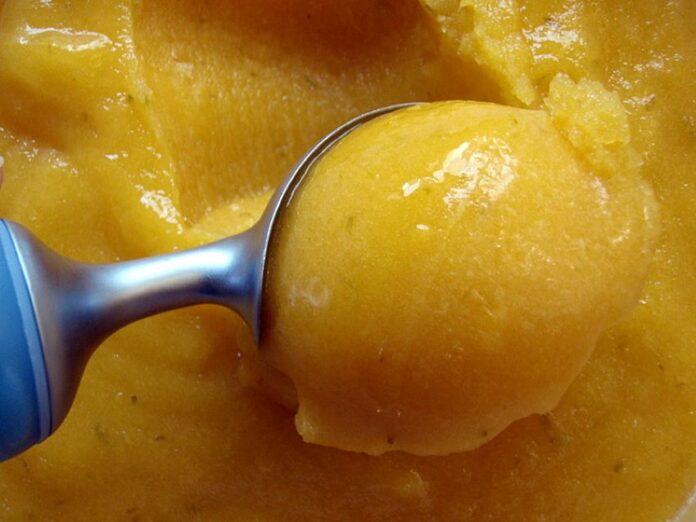 Closeup of ice cream scooper scooping mango sorbet