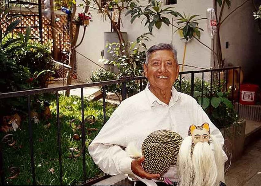 Manuel Jiménez Ramírez holding a pair of alebrijes while standing in a garden