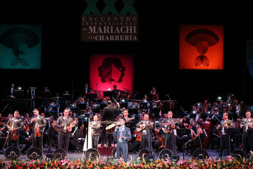 Mariachi musicians perform alongside an orchestra on a stage at the Mariachi and Charrería International Festival in Guadalajara